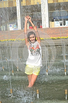 Cheerful girl dancing under jets of water in city fountain