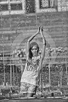 Cheerful girl dancing under jets of water in city fountain