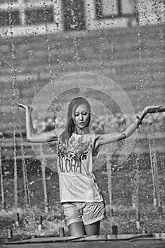 Cheerful girl dancing under jets of water in city fountain