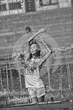 Cheerful girl dancing under jets of water in city fountain