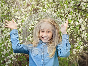 A cheerful girl in a denim shirt raised her hands up in the cherry orchard.