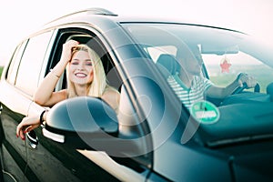 Cheerful girl is driving her new car with pleasure. The lady raises her elbow through the window and touching her hair gently