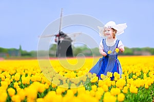 Cheerful girl in Dutch costume in tulips field with windmill