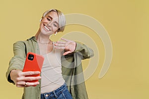 Cheerful girl in earphones waving hand while using mobile phone