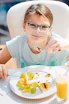 Cheerful girl eating pancakes, fresh fruits and drinking orange juice during breakfast. Healthy Lifestyle, Vegetarian Diet And