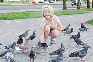 Cheerful girl feeds pigeons on the street in the city