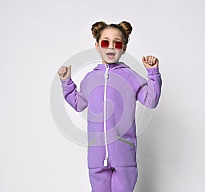 little preschooler girl in a warm blue sports overalls on a gray background. Cute little girl looking at the camera