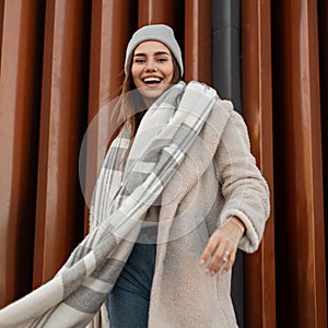 Cheerful girl with funny smile in trendy clothes outdoors. Positive young woman in coat in a knitted hat in a woolen vintage warm