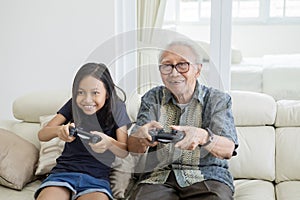 Cheerful girl and grandfather playing video games