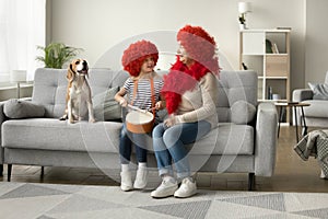 Cheerful girl and grandma in red wigs sitting with dog