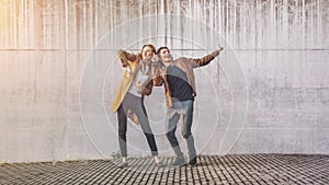 Cheerful Girl and Happy Young Man with Long Hair are Actively Dancing on a Street next to an Urban