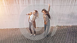 Cheerful Girl and Happy Young Man with Long Hair are Actively Dancing on a Street next to an Urban