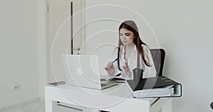 Cheerful girl having online communication on laptop at workplace in light office