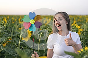 Cheerful girl holding windmill toy on field of sunflowers background. Green energy concept