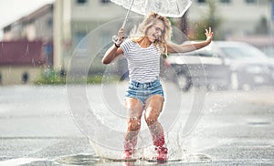 Cheerful girl jumping with white umbrella in dotted red galoshes. Hot summer day after the rain woman jumping and splashing in