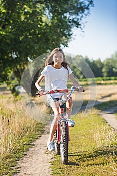 Cheerful girl with long hair riding her bicycle on dirt road at