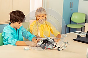 Cheerful girl looking at her classmate building a helicopter