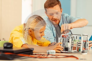 Cheerful girl looking at her teacher building a robot.