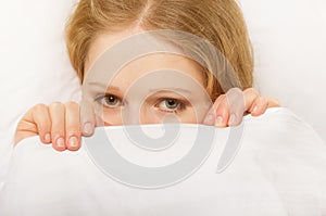 Cheerful girl looks out from under the blanket