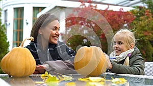 Cheerful girl and mom painting scary face on pumpkin, spend time together, fun