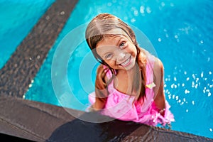 Cheerful girl in pink swimsuit enjoys summer day in outdoor childrens pool at resort. Kid smiles, swims, plays in water