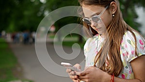 Cheerful girl playing games on phone in park. Playful girl using smartphone