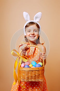 A cheerful girl with rabbit ears on her head with a basket of colored eggs in her hands
