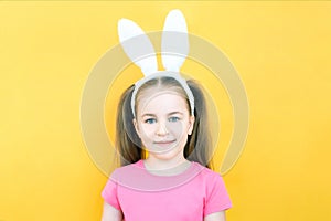 Cheerful girl with rabbit ears on her head on a yellow background. Funny crazy happy child. Easter child. Preparation for the