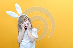 Cheerful girl with rabbit ears on her head on a yellow background. Funny crazy happy child. Easter child. Preparation for the