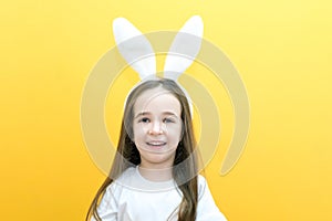 Cheerful girl with rabbit ears on her head on a yellow background. Funny crazy happy child. Easter child. Preparation for the