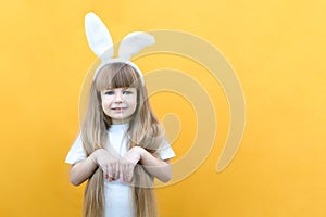 Cheerful girl with rabbit ears on her head on a yellow background. Funny crazy happy child. hands like a rabbit. Preparation for