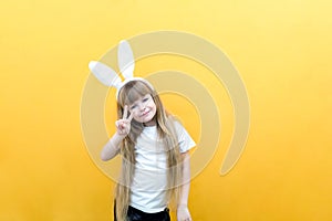 Cheerful girl with rabbit ears on her head on a yellow background. Funny crazy happy child. hands like a rabbit. Preparation for