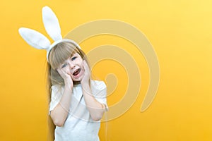 Cheerful girl with rabbit ears on her head on a yellow background. Funny crazy happy child. hands a rabbit. Preparation for the