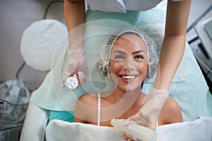 Cheerful girl is receiving facial treatment by beautician