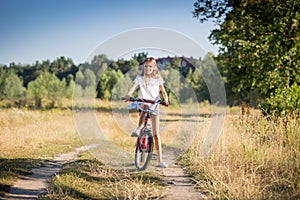 Cheerful girl riding bike in meadow at sunny day