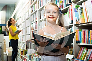 Cheerful girl in school age with book in bookstore