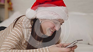 cheerful girl sends a message to the chat and laughs, merry christmas greetings, a teenager in a santa hat smiles
