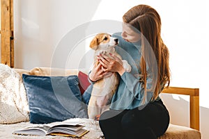 Cheerful girl sitting on bed and playing with puppy