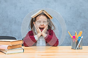 A cheerful girl sitting and holding a book over her head over a gray background. During this schoolgirl, her eyes closed