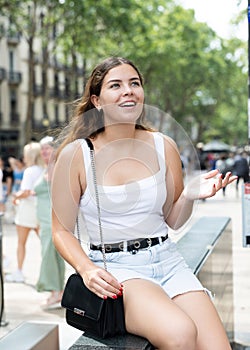 Cheerful girl sitting on La Rambla street during walk through summer Barcelona