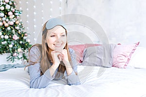 Cheerful girl in sleeping eye mask lying in bed in blue pajamas against