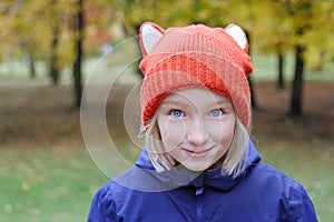 Cheerful girl smiling, the child is dressed in a funny knitted warm hat with ears, looks like a fox.