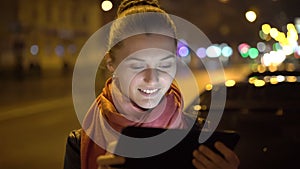 Cheerful girl smiling and using tablet on the night time on street. 4K