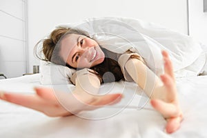 Cheerful girl stretching her arms in bed, waking up from good sleep or nap, enjoying the morning