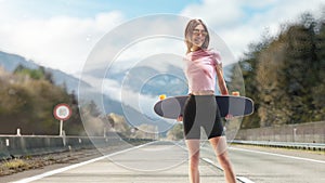 Cheerful girl with tattoos posing with a longboard while walking on the road. Sport emotion. Beautiful and fashion young