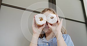 Cheerful girl teenager play with sweet donuts, cover eyes and smile