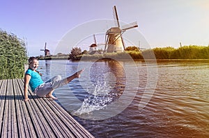 Cheerful girl  tourist splashing in the river on the beautiful landscape backgorund with old windmills in Netherlands