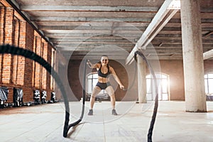 Cheerful girl training with battle rope at cross fit gym