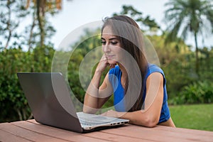 Cheerful girl watching online video on laptop computer sitting in the park