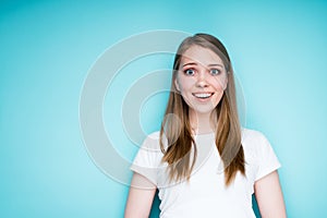 A cheerful girl in a white T-shirt is surprised and happy while standing on a blue background and opening her mouth photo